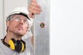 Man worker looks at the spirit level checks the wall with hard hat, glasses and ear protection headphones, white wall with copy Royalty Free Stock Photo