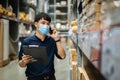 Man worker with medical mask talking on a mobile phone and holding clipboard to checking inventory in warehouse during coronavirus Royalty Free Stock Photo