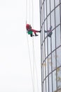 A man worker in red worksuit cleaning the exterior windows of a skyscraper - industrial alpinism at overcast weather -