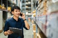 Man worker talking on a mobile phone and holding clipboard to checking inventory in the warehouse store Royalty Free Stock Photo