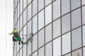 A man worker in worksuit cleaning the exterior windows of a skyscraper - industrial alpinism at overcast weather -