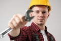 A man, a worker, in a yellow helmet, in a working overalls and a red checkered shirt, is holding a steel adjustable Royalty Free Stock Photo