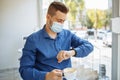 Man working from a cafe checking time on his watch and drinking coffee. Businessman wearing sterile medical mask leading matters Royalty Free Stock Photo