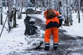 A man in working clothes with a shovel removes snow on the track in the park in winter