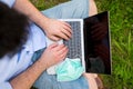 Man working with his laptop outdoors during Coronavirus pandemic. He has protective face mask.