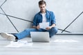 Man working at home. Handsome young man sitting on the floor and examining document while laptop and documents laying Royalty Free Stock Photo