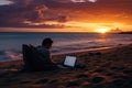 Man working on a laptop on the beach during a beautiful sunset, man lying on the sand of the beach with a laptop working at sunset