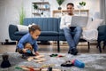 Man working on laptop while little boy playing with toys Royalty Free Stock Photo
