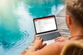 Man working on laptop by the pool while on vacation Royalty Free Stock Photo