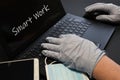 Man working on laptop and wearing latex gloves for virus prevention. Man working from home using smartphone and laptop. Royalty Free Stock Photo