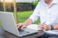 Man working on modern laptop sitting outside natural hardwood desk with green flora background sunlight day outdoor, everywhere Royalty Free Stock Photo