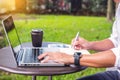 Man working on modern laptop sitting outside natural hardwood desk with green flora background sunlight day outdoor, everywhere Royalty Free Stock Photo