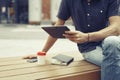 Man working outside in park using modern tablet, notebook, mobile phone. Wooden bench.