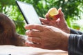 Man working on tablet computer with bitten apple in his hand. Wooden table. Green garden background. Royalty Free Stock Photo