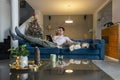 Man working on tablet in living room while his dog is lying next to him. The living room is decorated in the Christmas spirit Royalty Free Stock Photo