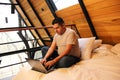 Man works as a digital nomad in the bed of a wooden cabin in the middle of the forest during his vacation