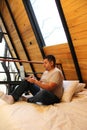 Man works as a digital nomad in the bed of a wooden cabin in the middle of the forest during his vacation