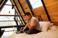 Man works as a digital nomad in the bed of a wooden cabin in the middle of the forest during his vacation