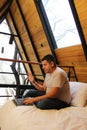 Man works as a digital nomad in the bed of a wooden cabin in the middle of the forest during his vacation