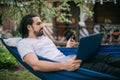 A man works with a laptop and a phone in a hammock in a country house Royalty Free Stock Photo