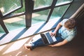 Man works with laptop sitting on the floor near the open window