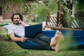 A man works with a laptop and smartphone in a hammock in a country house Royalty Free Stock Photo