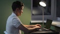 Man works on laptop typing on keyboard in semi-dark room Royalty Free Stock Photo