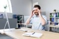 The man works in the office, the patient has a severe headache, upset businessman sitting at the table, holding his hands behind Royalty Free Stock Photo