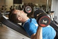 Man works out with dumbbells on a bench at a gym, side view Royalty Free Stock Photo