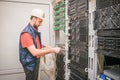 A man works in the server room of a data center. A technician connects a cable to a stack of managed switches. An engineer in a