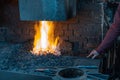 Man in a workshop, holding a metallic rod on flames, making fire