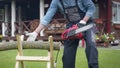 Man in workwear saws firewood on sawhorses with an electric saw at his home site
