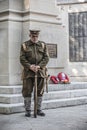 A man in World war one soldiers uniform standing next to a British war memorial with red