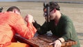 Man wrestling with man in mask on wooden fretted table on beach