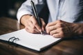 Man writes on empty notebook page with pen sitting at wooden table in room closeup