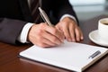 Man writes on empty notebook page with pen sitting at wooden table in room closeup