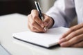 Man writes on empty notebook page with pen sitting at wooden table in room closeup