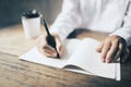 Man writing in blank diary and paper coffee cup on wooden table