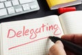 Man is writing delegating in the notepad. Delegate concept.