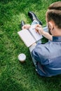 Man writing on notebook and drinking coffee from paper cup while sitting on green grass Royalty Free Stock Photo