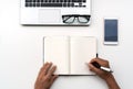 Man writing on notebook with mobile phone, computer and glasses on white table, top view, copy space for text Royalty Free Stock Photo