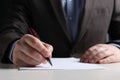 Man writing on sheet of paper with pen at white wooden table, closeup Royalty Free Stock Photo