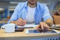 Man writing work plan with pen on paper notebook, browsing internet on digital tablet on office desk Royalty Free Stock Photo