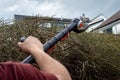 Man& x27;s arm holding battery powered hedge trimmers to clip branches and leaves from overgrown hedge. Royalty Free Stock Photo