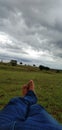 A man& x27;s feet sleeping on the green grass and the black cloud and the white clouds and the tree beautiful nature