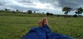 A man& x27;s feet sleeping on the green grass and the black cloud and the white clouds