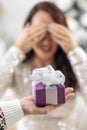 Man's hand is holding purple Xmas present with a ribbon in front of a woman closing her eyes with hands Royalty Free Stock Photo