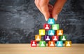 man& x27;s hand holding a top of wooden blocks pyramid with people icons over wooden table