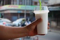 Man& x27;s hand holds cold milk blended into clear plastic glasses with optional focus plastic straws. Street food concept.