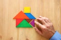 man& x27;s hand pointing at house made from tangram puzzle over wooden table. Royalty Free Stock Photo